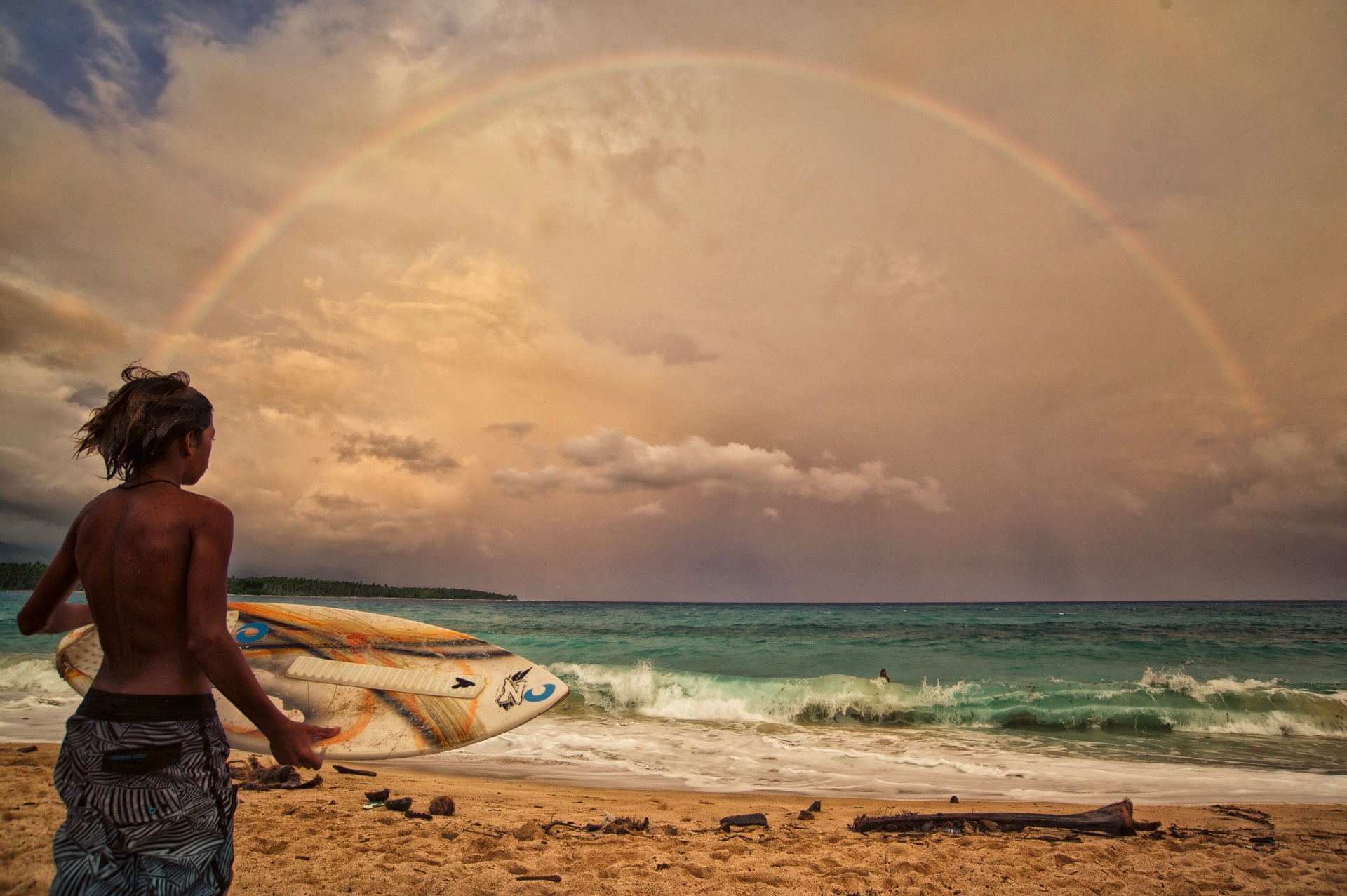 Surfer watching a rainbow arch over the ocean — captured by Pastor Wood
